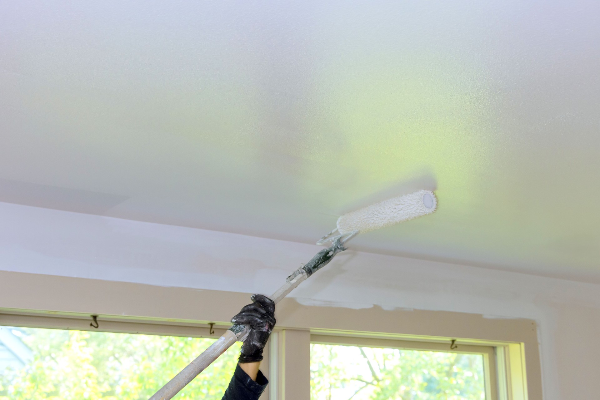 Painting ceiling with roller brush in bright room during works day